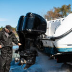 Caucasian man pressure washing outboard motors on power boat