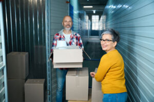 Adult man carries a cardboard box with things while a woman looks at the camera