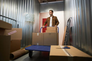 Pensive man pushing cart with belongings inside storage unit