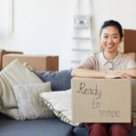 favorite_borderfilter_none Portrait of young Asian woman holding cardboard box with ready to move inscription and smiling looking at camera