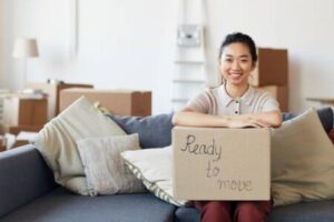 favorite_borderfilter_none Portrait of young Asian woman holding cardboard box with ready to move inscription and smiling looking at camera