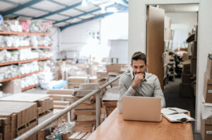Manager working while sitting in an overcrowded warehouse office