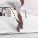 Yacht maintenance. A man polishing side of the white boat by grinder machine in the marina