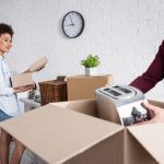 Happy young man packing box with toaster near smiling girlfriend