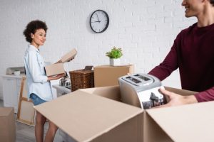 Happy young man packing box with toaster near smiling girlfriend