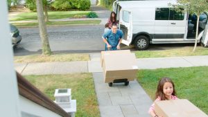 Children helping parents unload boxes from van on family moving in day